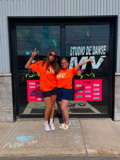 Deux femmes en t-shirts orange devant un studio de danse.