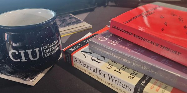 A mug from Columbia International University beside a stack of academic books.
