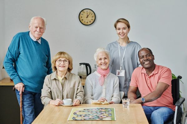 Group of smiling elderly people and a caregiver around a table with a board game.