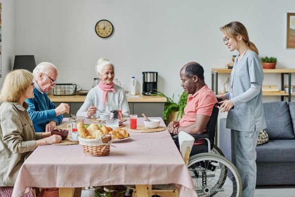Group of elderly people having breakfast with caregiver assistance.