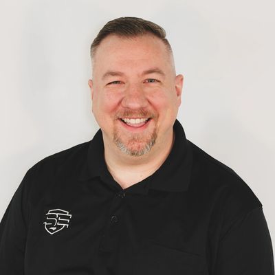 Smiling man in black polo with logo on white background.
