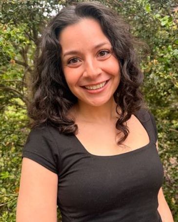 Smiling woman with curly hair in a black top outdoors.