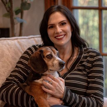A woman smiling while holding a dog on a couch.