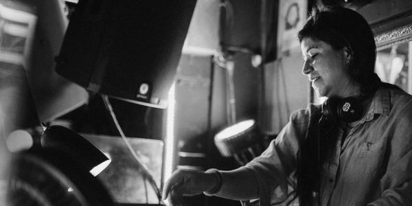 A female DJ mixing music in a dimly lit room with headphones around her neck.