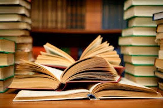 Three open books on top of a desk with stacks of books beside them. 