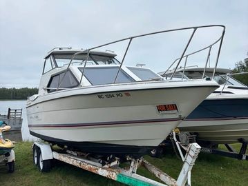 White cabin cruiser boat on a trailer by the water.