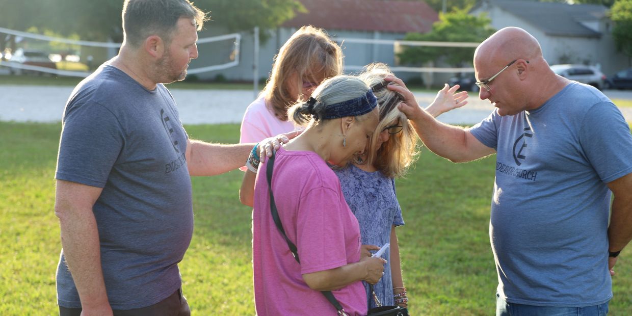 A group of people praying together outside on a sunny day.