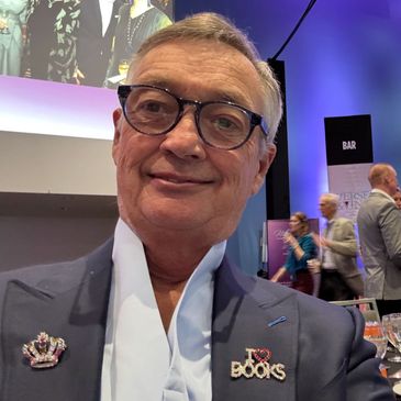 Smiling man wearing glasses with book-themed pins at an event.