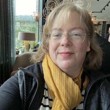 A woman wearing glasses and a yellow scarf indoors.
