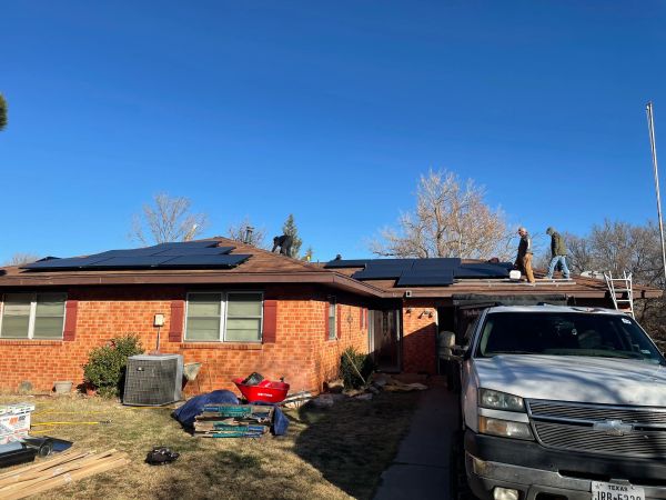 Workers installing solar panels on a brick house roof under clear sky.