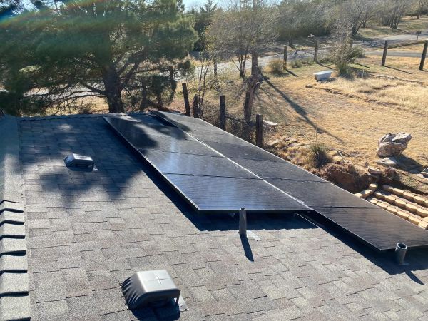 Solar panels installed on a residential rooftop in a sunny, wooded area.