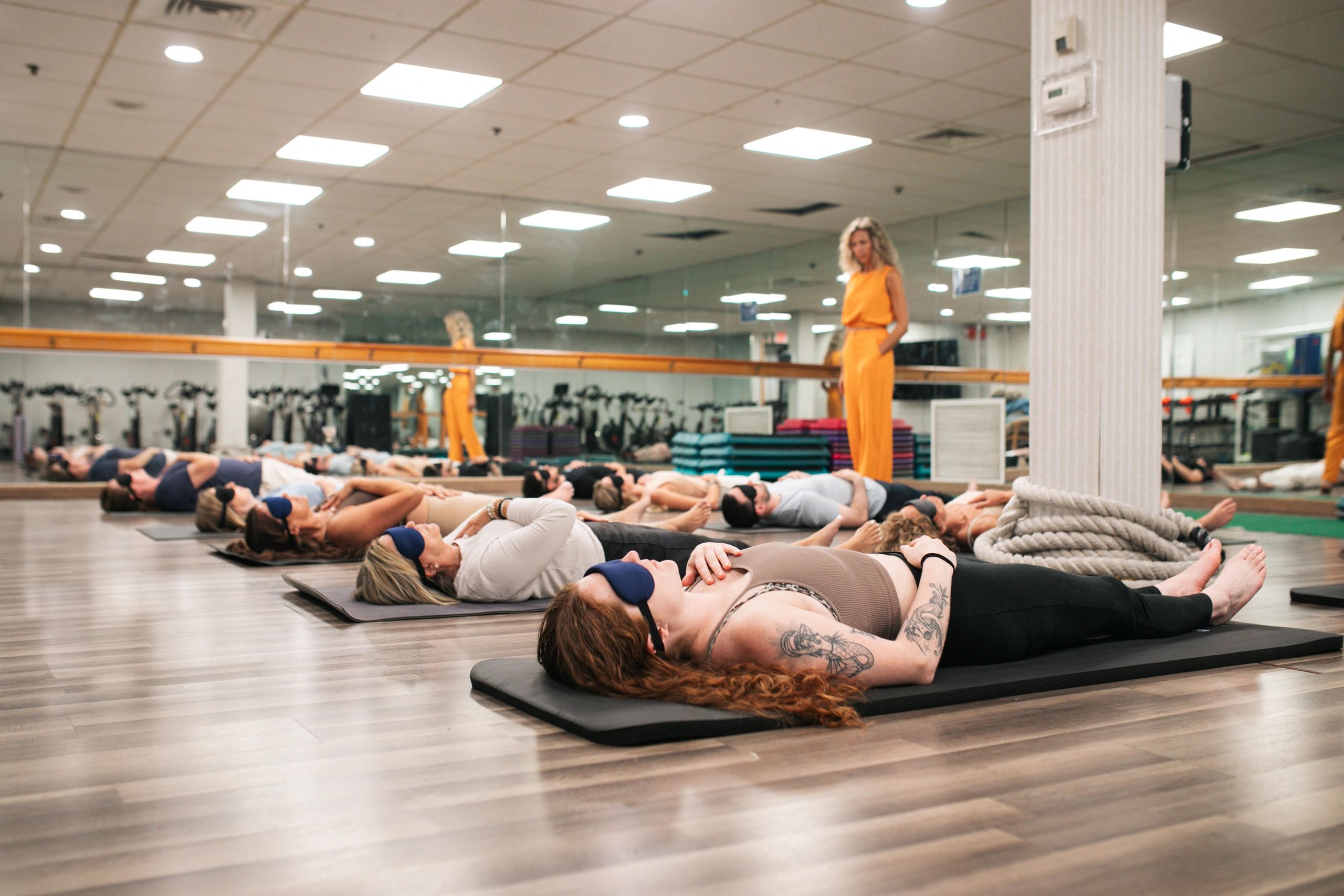Group meditation session with participants lying on mats wearing eye masks.