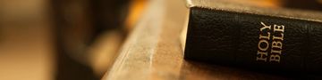 Close-up of a Holy Bible on a wooden surface with warm lighting.