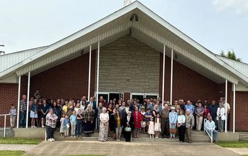 Large group of people gathered outside a brick building, likely for a community or family event.