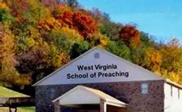 Building with a sign reading 'West Virginia School of Preaching' against autumn foliage.