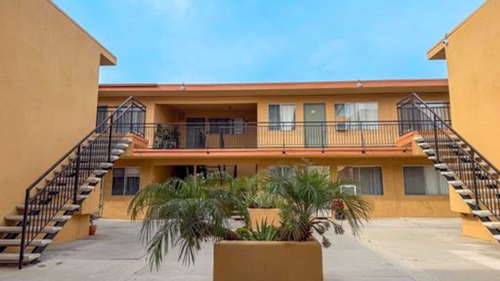 Two-story orange apartment complex with outdoor staircases and potted plants.