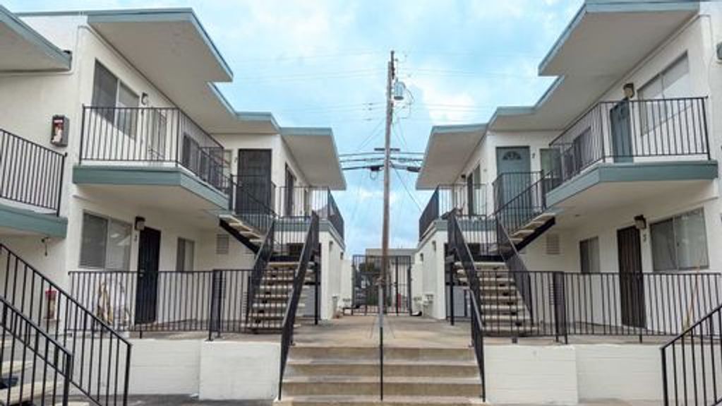Symmetrical view of two-story apartment buildings with exterior staircases and balconies under a cloudy sky.