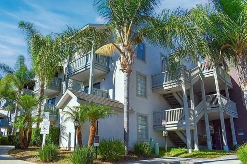 Modern apartment building with palm trees and balconies under a clear blue sky.