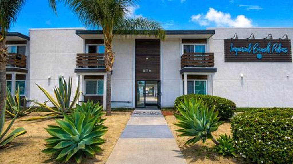 Modern apartment building with tropical landscaping and clear blue sky.