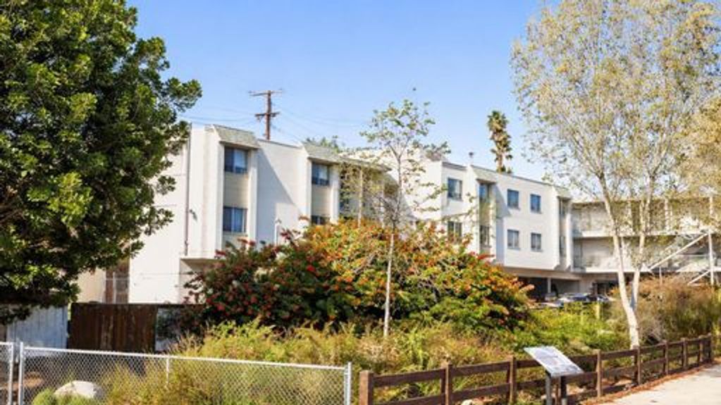 Residential building with trees and greenery in front under a clear blue sky.