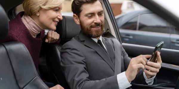 Two people inside a car looking at a phone, smiling.
