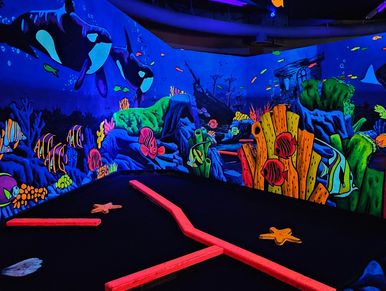 Glowing underwater-themed mini golf course with vibrant marine life murals.