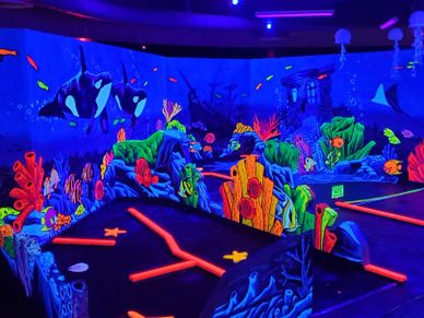 A vibrant underwater-themed mini golf course with glowing neon corals and sea creatures.