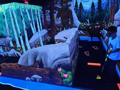 Person playing blacklight mini golf with nature-themed obstacles.