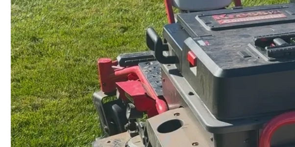 A robotic lawn mower with red handles on a green lawn.