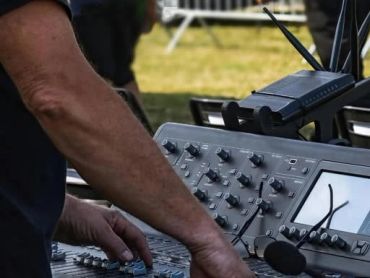 Person adjusting controls on an audio mixing console outdoors.