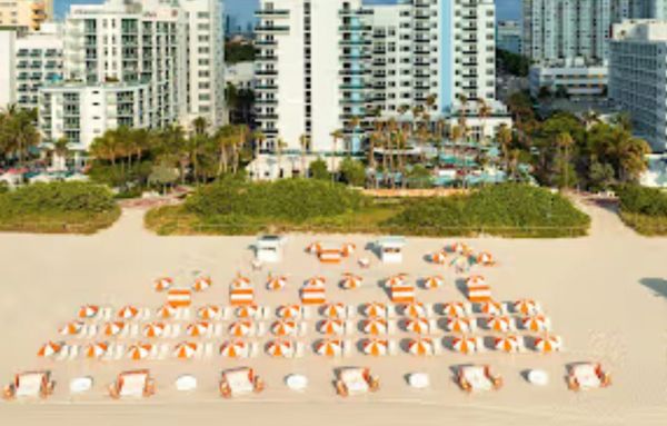 Aerial view of a beach with orange and white umbrellas in front of tall buildings.
