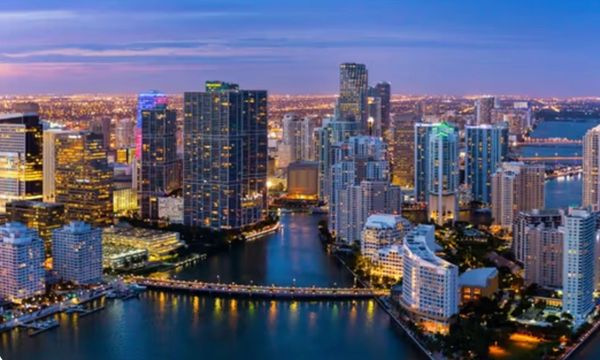 A vibrant city skyline at dusk with illuminated buildings and waterways.