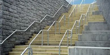 Wooden stairs with multiple metal railings alongside a stone wall.