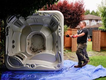 Man installing or moving an empty hot tub in a backyard.