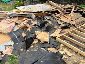 Pile of construction debris including wood, insulation, and roofing materials.