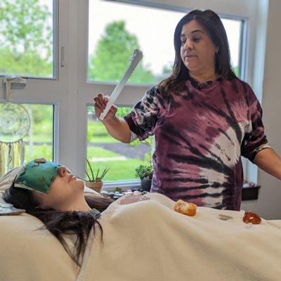 A woman performs a healing ritual on a person lying down with crystals on them.