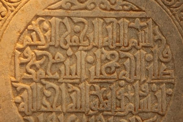 Intricate Arabic calligraphy carved in stone with decorative patterns.