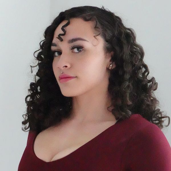 Confident woman with curly hair wearing a maroon top.