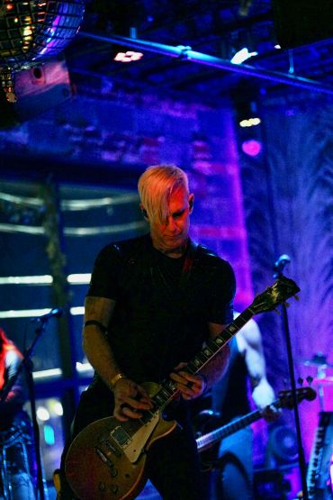 Guitarist playing on stage in blue-purple lighting.