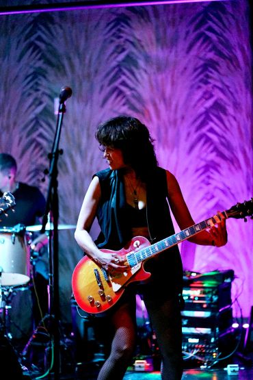 Female guitarist playing on stage with purple lighting.