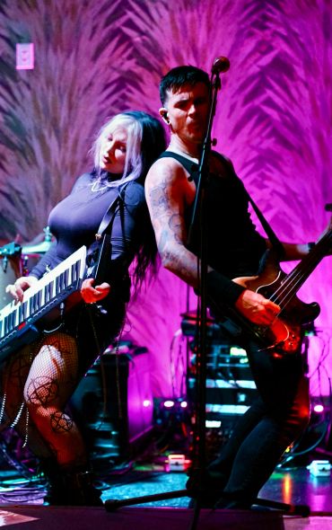 Two musicians playing keytar and bass on vibrant stage.