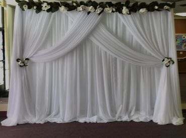 Elegant white draped backdrop with flowers.