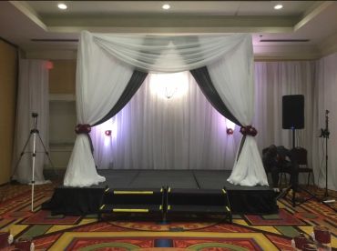 Small stage with white and black draped arch in a decorated room.