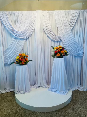 Elegant white draped backdrop with floral arrangements.