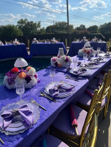 Elegant outdoor table setting with purple theme and floral centerpieces.