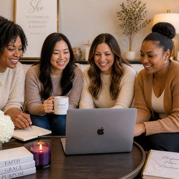 Four women smiling and watching a laptop together in a cozy room.