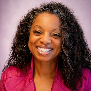 Smiling woman with curly hair wearing a magenta jacket.