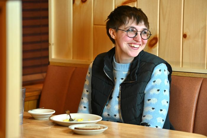 Image of Vanessa, sitting at a table in a diner, smiling and looking off camera.