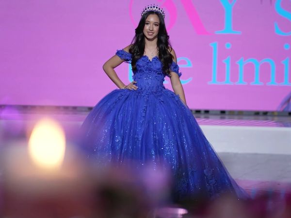 Young woman in a sparkling blue ball gown and tiara on stage.