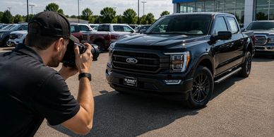 A person photographing a black Ford pickup truck outdoors.